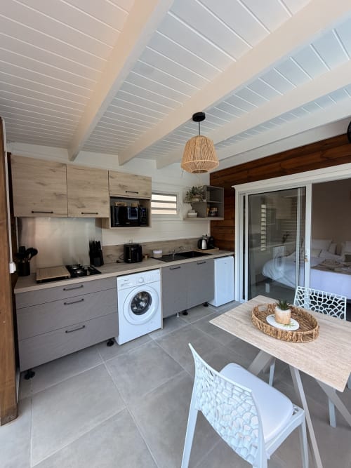 Modern cottage kitchen at Filao in Sainte-Rose with white beamed ceiling, gray cabinetry, dining area, and bedroom entrance