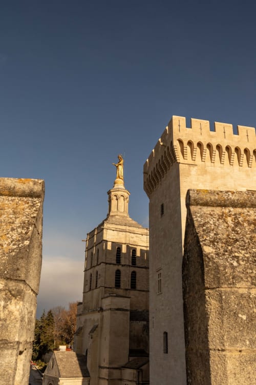 Medieval stone fortress with golden statue atop bell tower, Le Prieuré Notre-Dame in Montfrin, France