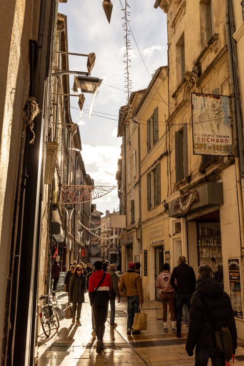 Historic European alley with pedestrians near Montfrin, France, featuring yellow stone buildings and vintage signage