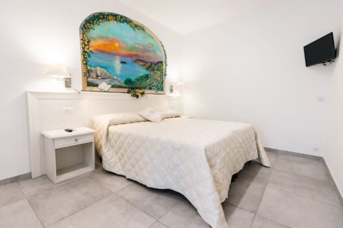 Bright bedroom at L'Amaranto BnB in Agerola with white bed, coastal sunset mural, and TV