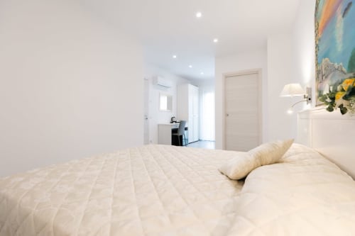 Bright, minimalist bedroom at L'Amaranto B&B in Agerola with cream bedding, white furnishings, and modern amenities