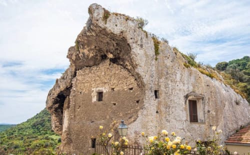 Casa vacanze in pietra storica a Valledoria, arroccata sulla scogliera con fiori gialli e splendida vista sulla valle
