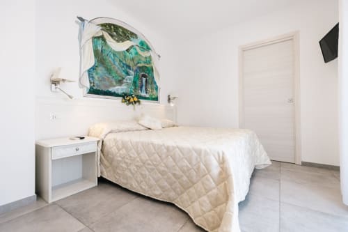 Camera luminosa all'L'Amaranto B&B di Agerola con letto trapuntato beige, comodino bianco e opere d'arte naturale sopra la testata