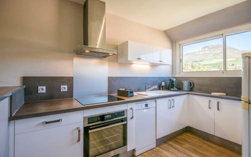 Modern bright kitchen in Millau apartment with white cabinetry, dark countertops, stainless steel appliances, and mountain