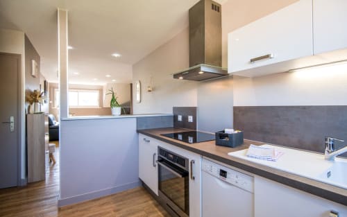 Modern kitchen with white cabinets, dark countertop, gas range, and island in bright Millau apartment with city views