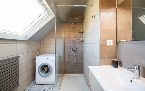 Modern bathroom in Millau apartment with walk-in shower, washing machine, and sink under skylight