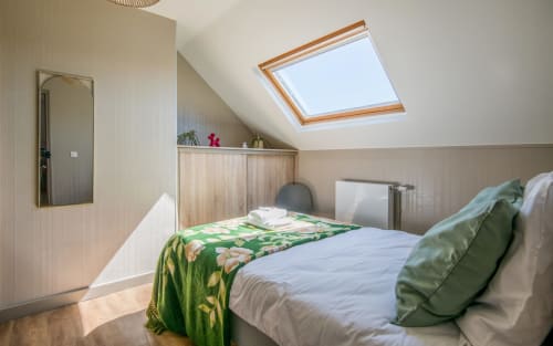 Bright attic bedroom in Millau apartment with skylights, green floral bedding, and wooden furniture