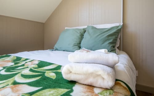 Made bed with white sheets, green pillows, and folded towels at Appt Alba apartment in Millau