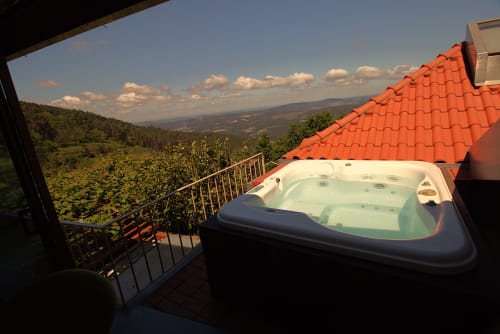 Hot tub on terrace with red roof at Pera da Serra guesthouse in Lousã, Portugal, overlooking forested valley