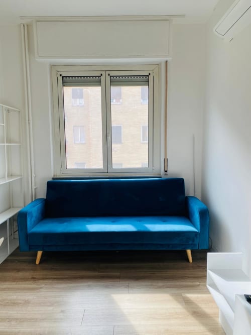 Modern blue velvet sofa with wooden legs in bright Milano Underground apartment, natural light from double windows