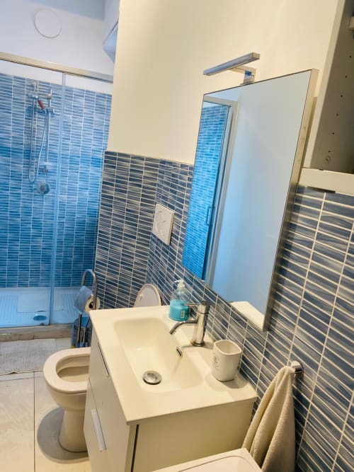 Modern bathroom in Milano Underground BnB with blue tile walls, white sink, mirror, toilet, and shower area