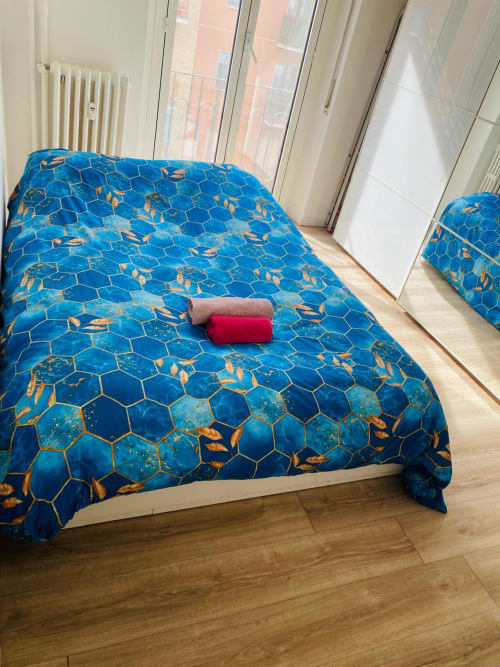 Bright bedroom at Milano Underground BnB with blue geometric bedspread, rolled towels, hardwood floor, and balcony doors