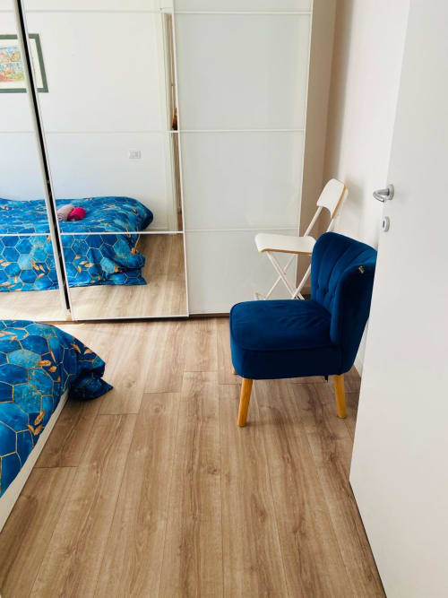 Modern bedroom in Milano Underground apartment with blue geometric bedding, dark blue velvet chair, wooden flooring, and