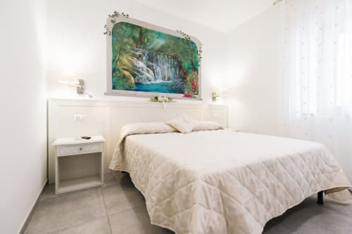 Clean modern bedroom at L'Amaranto B&B in Agerola with white bedding, nightstand, and waterfall artwork above headboard