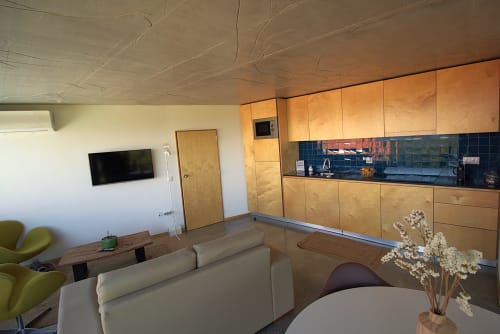 Modern apartment kitchen and living area with wooden cabinetry, blue tile backsplash, cream sofa, and TV at Pera da Serra