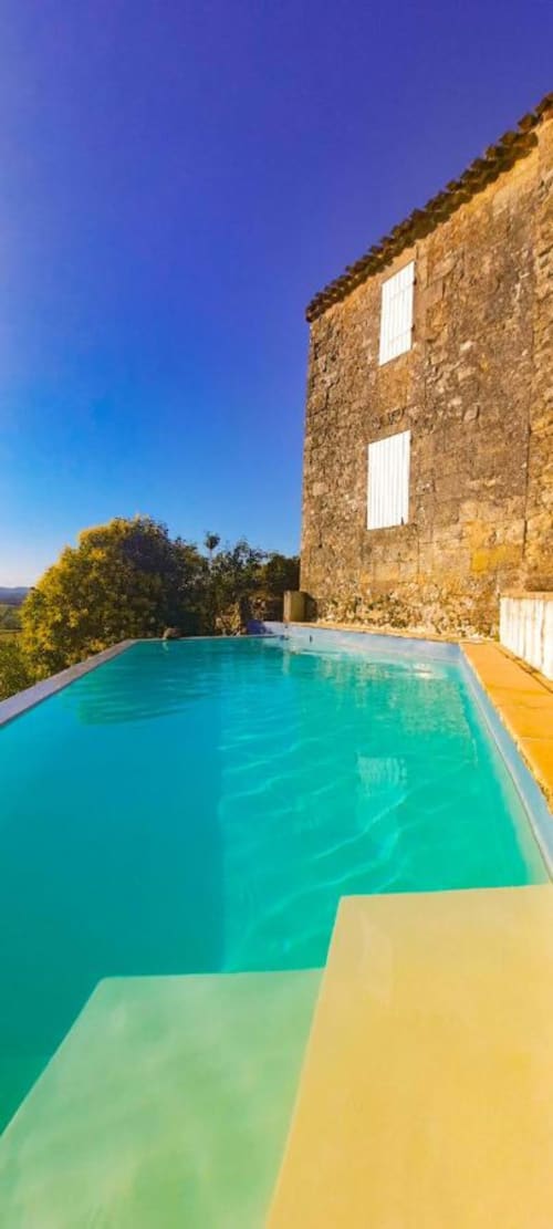 Turquoise pool with yellow deck at Le Prieuré de Saint-Pierre, Saint-Pey-de-Castets, beside stone building