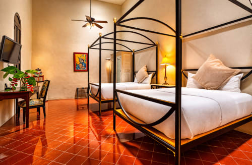 Luxury bedroom at Villa Merida with twin four-poster beds, terracotta floors, and warm lighting in Merida, Mexico