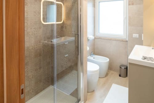 Moderno bagno nella Suite Flavia Deluxe presso EQM Roma con doccia in vetro, bidet, toilette e specchio illuminato