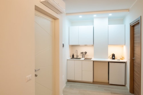 Modernissima angolo cottura nella Suite Flavia Deluxe di EQM Roma, con cabinetry bianca e elettrodomestici in acciaio inox