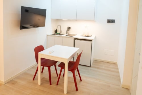 Kitchenette della Suite Ottavia Deluxe presso EQM Roma con tavolo da pranzo, sedie rosse e cucina compatta