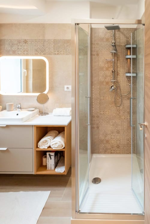 Bagno moderno nella EQM Roma Suite Ottavia Deluxe con doccia in vetro, lavabo bianco, specchio illuminato e mobile in legno