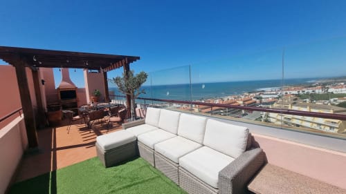 Terraço na cobertura da King's House Ericeira com vista de mar, sofá branco, área de refeições ao ar livre e vila costeira ao fundo