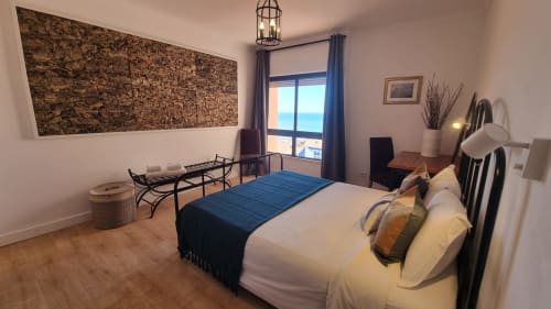 Quarto moderno no apartamento King's House Ericeira com vista para o mar, roupa de cama branca, manta azul, arte em cortiça na parede e