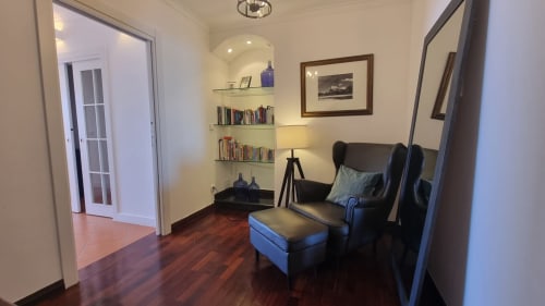 Sala de estar moderna na King's House Ericeira com poltrona de couro escuro, puf, prateleiras embutidas e piso de madeira