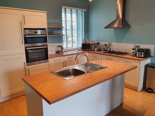 Modern kitchen with wood countertops, island sink, stainless steel appliances, and turquoise walls at Beach House cottage.