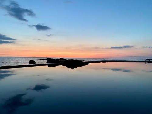Serene coastal sunset reflection at 2 Doves Holiday Property near Exeter with calm waters and rocky shoreline
