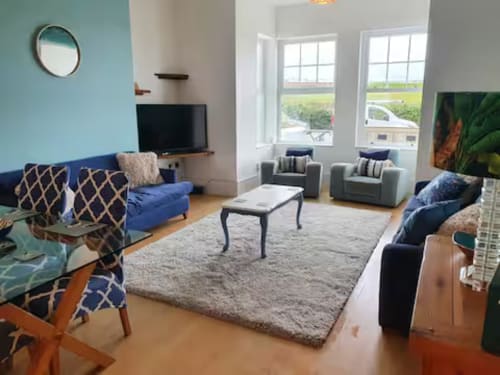 Modern living room at 2 Doves Holiday Property in Exeter with blue patterned chairs, gray armchairs, TV, and countryside