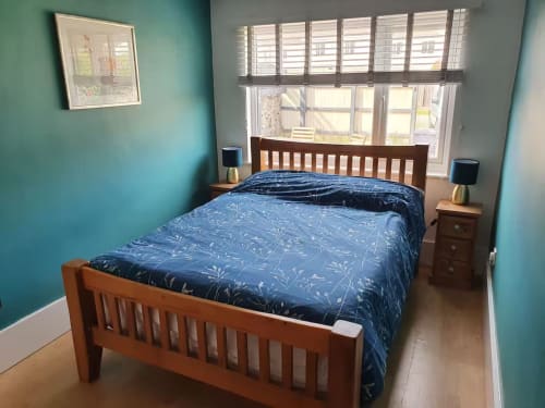Bright turquoise bedroom with wooden bed frame, blue bedding, and large window at 2 Doves Holiday Property, Exeter