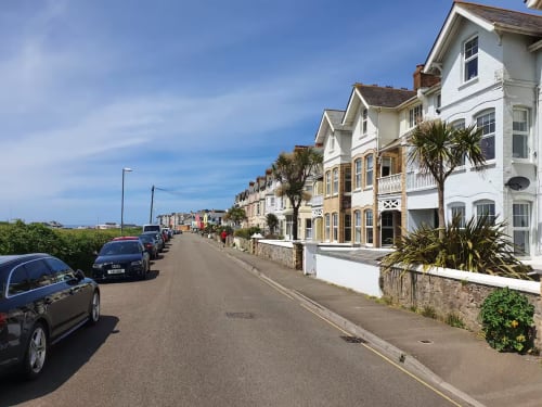 Row of white Victorian seafront villas with parked cars on quiet residential street in Exeter, GB