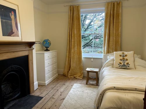 Cozy bedroom at 2 Doves Holiday Property in Exeter with fireplace, cream bedding, gold curtains, and wooden flooring