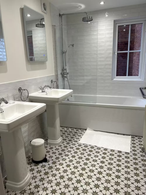 Modern bathroom at 2 Doves Holiday Property in Exeter with dual sinks, bathtub, shower, and patterned floor tiles