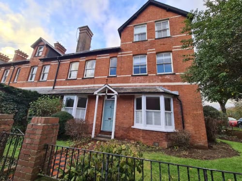 2 Doves Holiday Property in Exeter: Victorian brick building with white windows and light blue door, ivy-covered walls, and