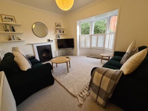 Bright living room at 2 Doves Holiday Property in Exeter with black armchairs, fireplace, TV, and garden views