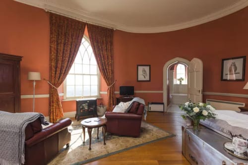 Elegant bedroom at 2 Doves Holiday Property in Exeter with terracotta walls, burgundy leather seating, and arched doorway