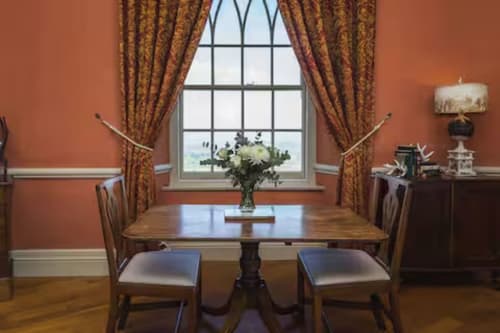Elegant dining room at 2 Doves Holiday Property in Exeter with terracotta walls, wood table, and gold curtains overlooking