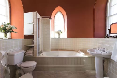 Luxurious bathroom at 2 Doves Holiday Property in Exeter with terracotta walls, curved bathtub, and pedestal sink