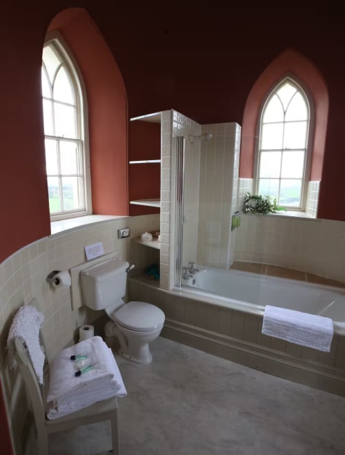 Luxurious bathroom at 2 Doves Holiday Property, Exeter with twin arched windows, bathtub, shower enclosure, and cream tile