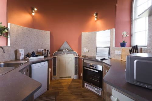 Modern kitchen at 2 Doves Holiday Property in Exeter with orange walls, stainless steel appliances, and wooden flooring