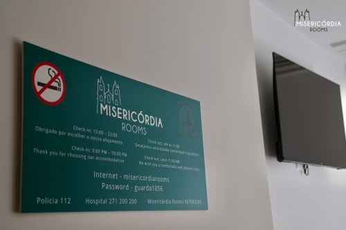 Placa informativa do hotel Misericórdia em Guarda com detalhes de check-in, WiFi e informações de contato em parede azul-petróleo