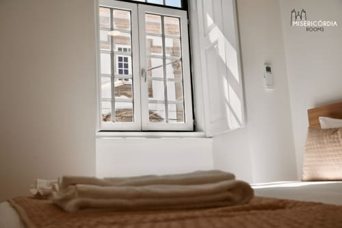 Quarto moderno e luminoso na Misericórdia Rooms em Guarda com grandes janelas, toalhas dobradas, piso de madeira e vistas da cidade.