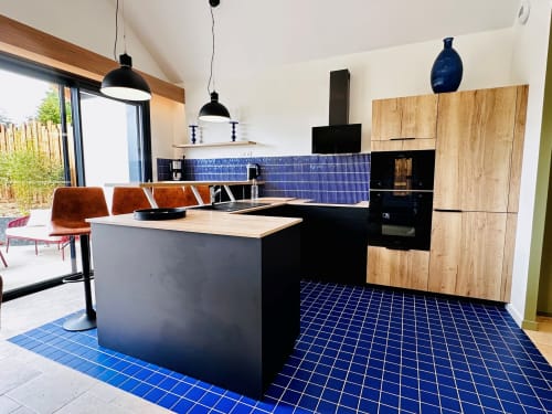 Cuisine moderne du L'Instant Cottage avec carrelage bleu, îlot noir, mobilier en bois et vue sur le jardin du gite près d'Amboise