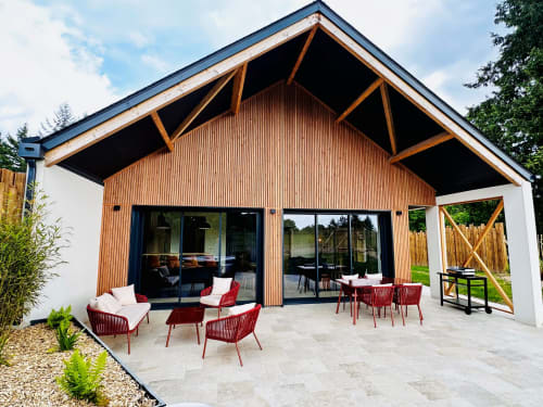 Terrasse du cottage L'Instant au design moderne, accents en bois, chaises rouges et vue sur le jardin à Amboise, France