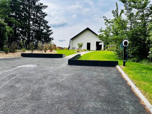 Maison blanche moderne aux portes noires à L'instant Cottage près d'Amboise, entouré de pelouse verte et d'arbres, avec allée pavée et borne de recharge