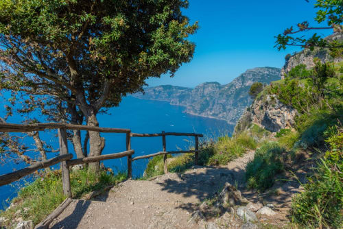 Coastal hiking trail with wooden railing overlooking turquoise sea near L'Amaranto in Agerola, Italy