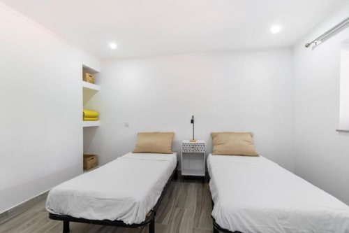 Quarto duplo na Villa Principezinho BnB Portugal com paredes brancas, duas camas individuais, almofadas douradas e prateleiras minimalistas