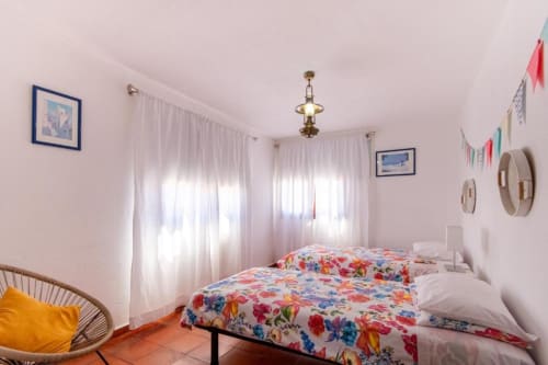 Quarto claro da Villa Principezinho com camas gêmeas, roupa de cama floral, cortinas brancas e pisos em terracota português
